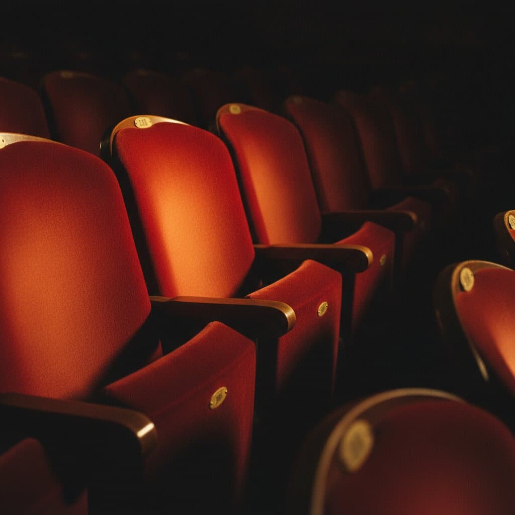 Leere rote Theaterstuhlreihen im Halbdunkel mit kleinen Messingschildern an den Seitenplätzen